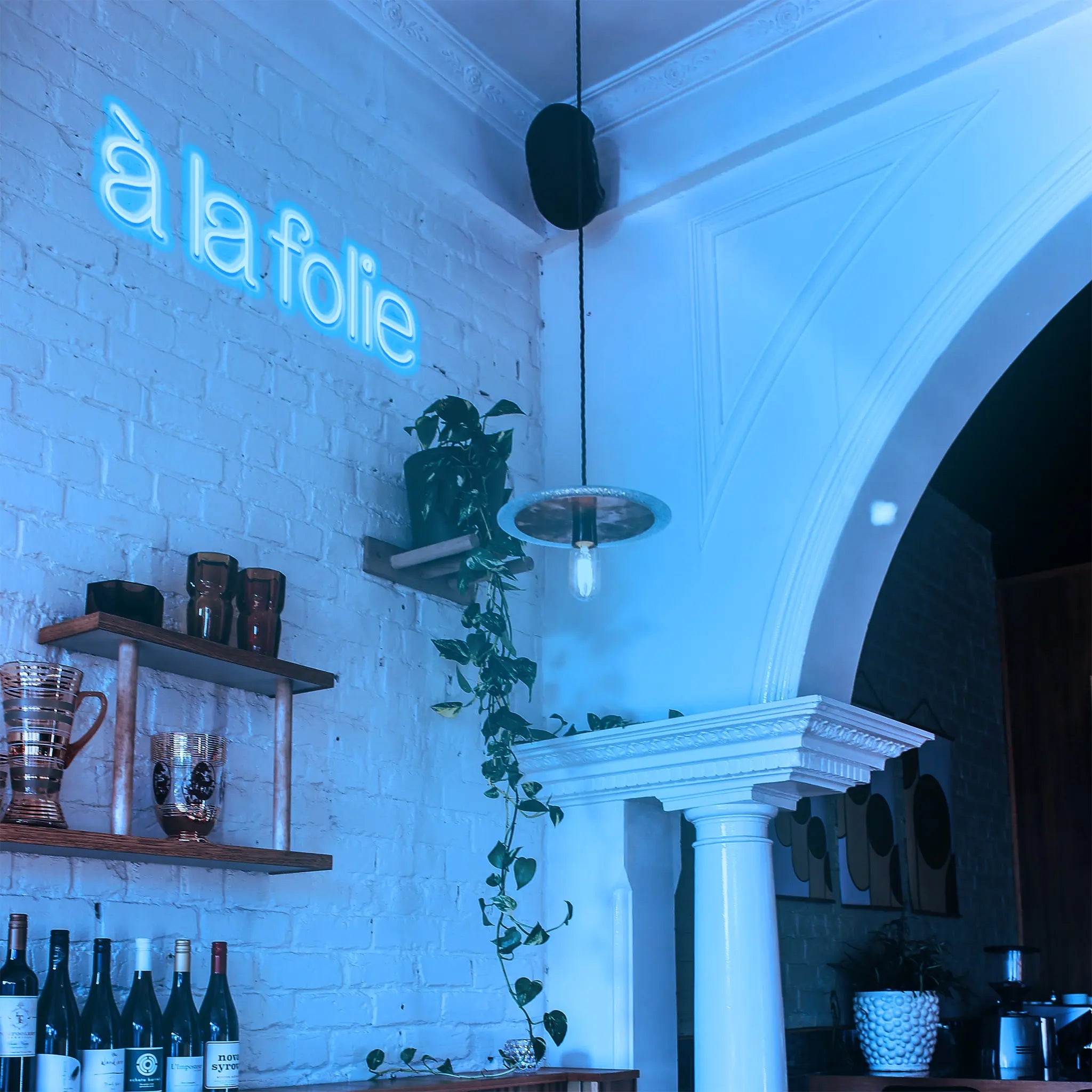 À la Folie Neon Sign mounted in a living room, creating a playful and romantic atmosphere with its warm neon glow.